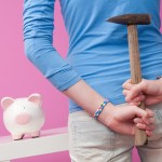 Young woman with hammer behind back thinking about smashing her piggy bank