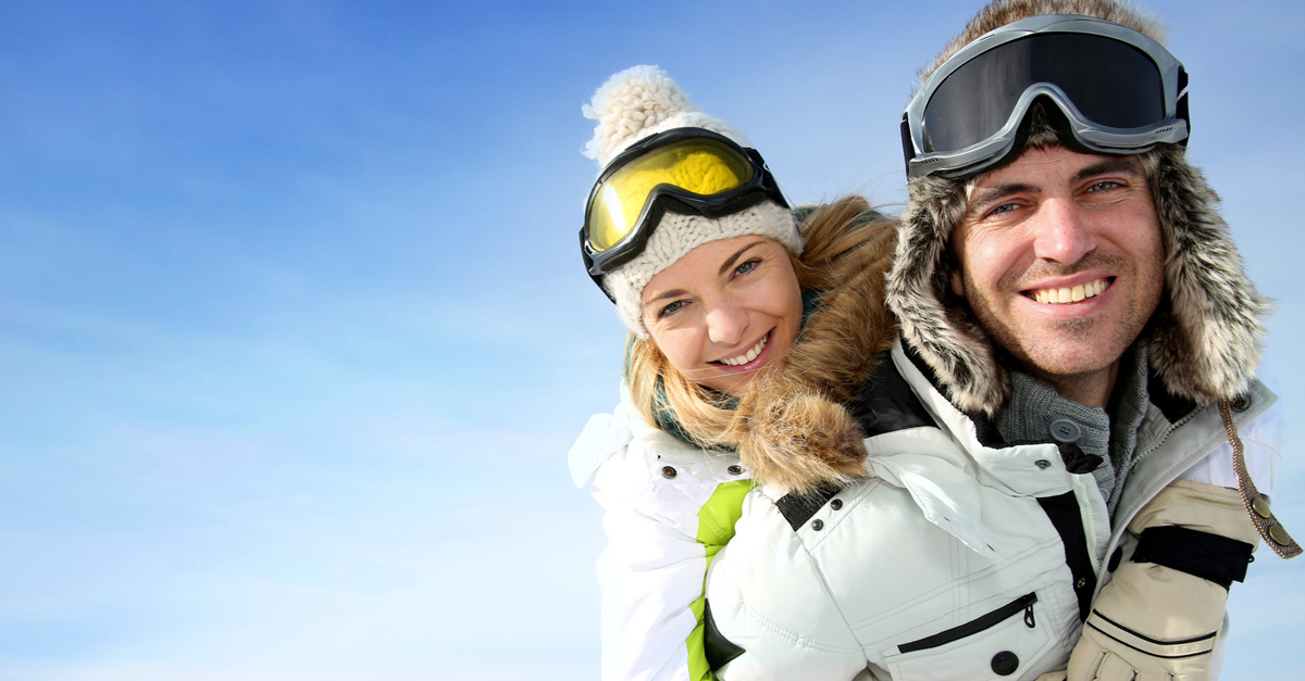 Young man in snow gear with his girlfriend on his back on a snowy mountain