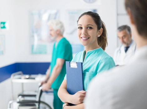A smiling nurse holding a clipboard in a busy hospital, representing healthcare workers who may benefit from home loans for healthcare workers.