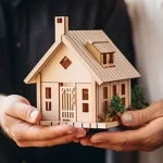 Two people holding a small model house together, symbolising home ownership,