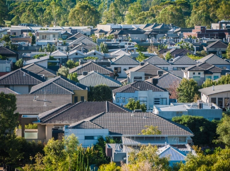 An aerial view of a suburban neighbourhood featuring a variety of modern houses with tiled roofs and lush greenery. The dense cluster of homes is surrounded by trees, creating a picturesque and serene residential area.