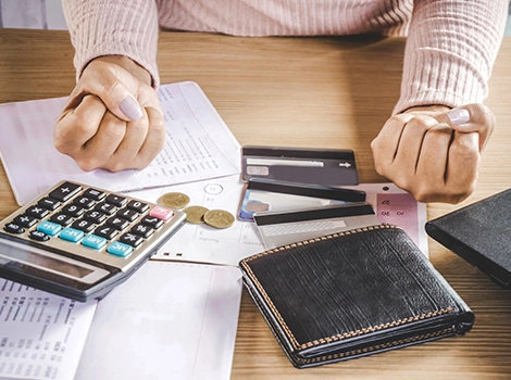 A person clenches their fists over a stack of financial documents, a calculator, and several credit cards. Coins and a wallet are placed nearby, suggesting financial stress. The image implies the relief of Waived Lenders Mortgage Insurance (LMI).