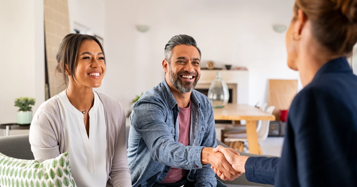 Smiling couple shaking hands with a professional, representing trust and partnership in achieving their homeownership goals through expert mortgage advice.