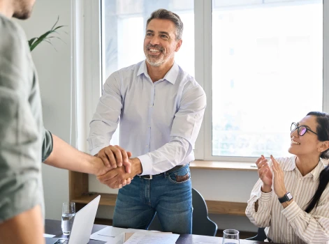 Professional mortgage broker in Melbourne shaking hands with a client during a meeting, with a team member clapping in agreement, showcasing trust and expertise in home loan services.