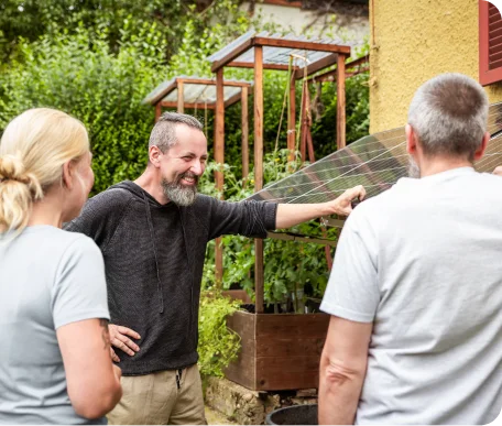 Smiling man explaining solar panel installation to a couple in a lush backyard garden, showcasing how they used solar panels to secure lower mortgage rates.