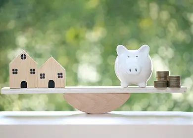 Scale with houses on one side and piggy bank with coins on the other, showing financial balance.