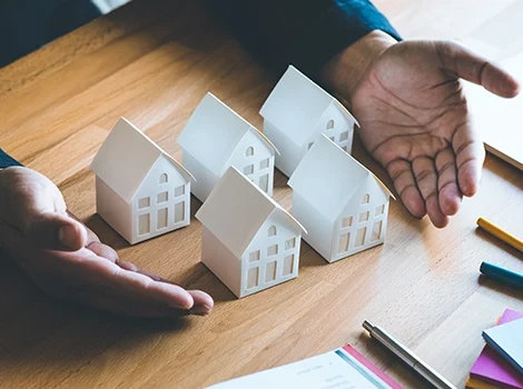 A person’s hands presenting small white house models, symbolising investment loans for real estate.