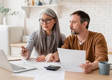 Two individuals reviewing financial documents at a table with a laptop, pen, and calculator, discussing rental yield.